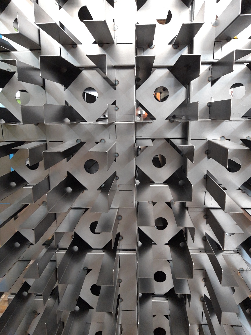 Stacks of fabricated sheet metal components on wooden pallets inside a workshop with safety signs on the wall